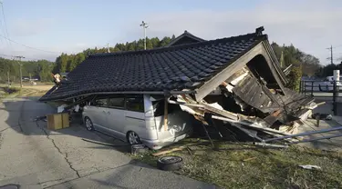 Sebuah kendaraan berada di bawah sebuah bangunan yang runtuh akibat gempa bumi di Shikamachi, prefektur Ishikawa, Jepang, Selasa (2/1/2024). (Kyodo News via AP)