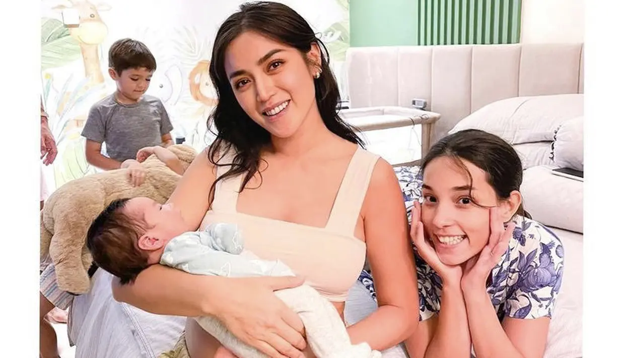 Menggendong bayi dari sang kaka, Jessica tampak glowing mengenakan crop top warna nude dipadukan loose pants.