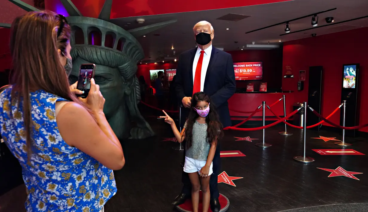 Seorang anak berfoto dengan sosok Donald Trump yang bermasker saat Madame Tussauds New York dibuka kembali di New York City, Kamis (27/8/2020). Patung lilin Donald Trump akan berada di pintu masuk untuk mengingatkan tentang protokol kesehatan, termasuk mengenakan masker. (Cindy Ord/Getty Images/AFP)