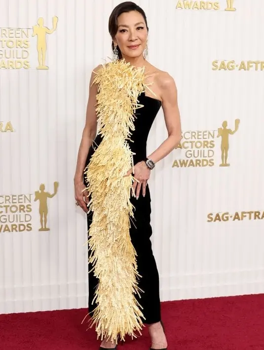 Michelle Yeoh tampil menawan di usia 60 tahun berbalut gaun hitam berdetail gold fringe dari Schiaparelli.  [@parademag].
