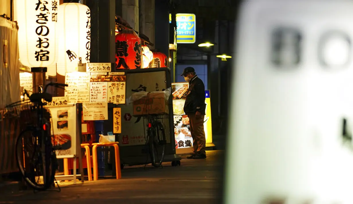 Seorang pria yang mengenakan masker pelindung untuk membantu mengekang penyebaran COVID-19 berdiri di sebuah bar di Tokyo, Jepang, Kamis, (4/2/2021). Tokyo mengonfirmasi lebih dari 730 kasus baru COVID-19 pada 4 Februari 2021. (AP Photo/Eugene Hoshiko)