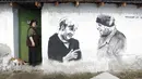 Ivanka Toneva memasuki halaman rumahnya di sebelah mural yang menggambarkan sang suami, Krustyo Tonev yang sedang berbincang dengan Kanselir Jerman, Angela Merkel, di desa Staro Zhelezare, Bulgaria, Kamis (27/7). (AP Photo/Valentina Petrova)