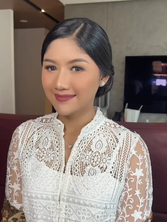 Rambutnya pun disanggul minimalis dengan rapi. Ia terlihat mengenakan aksesori perhiasan anting minimalis dan kalung berliontin E. [@fidelhertamakeup]
