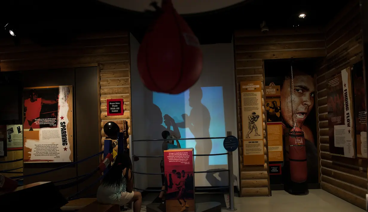 Pengunjung menyaksikan anaknya meniru gaya Muhammad Ali di Muhammad Ali Center, Louisville, Kentucky (5/6). Ali wafat pada usia 74 tahun di Rumah Sakit Kota Phoenix, Arizona, AS, Sabtu (4/6). (AFP PHOTO/Brendan Smialowski)