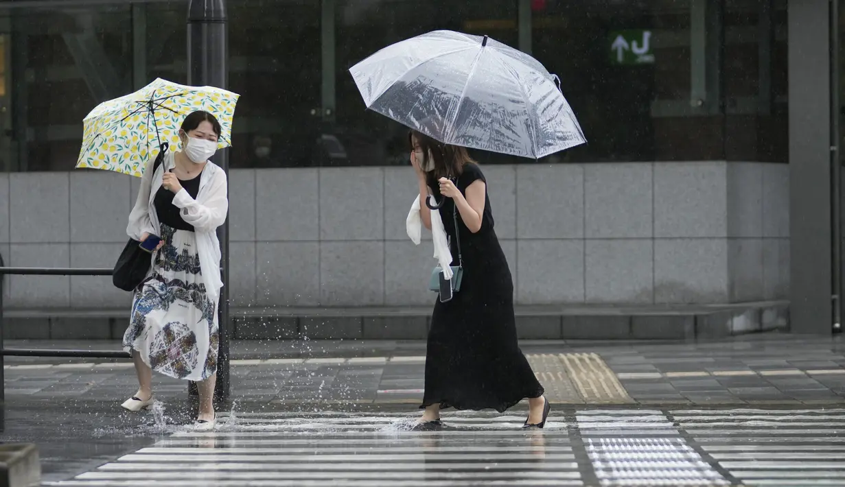 Para perempuan bereaksi saat mereka mengarungi genangan air di persimpangan di tengah hujan di Tokyo, Selasa (20/9/2022). Topan Nanmadol melanda Jepang selama akhir pekan sebelum melemah saat bergerak ke utara. Sejumlah kerusakan baru dilaporkan di Jepang selatan. (AP Photo/Hiro Komae)