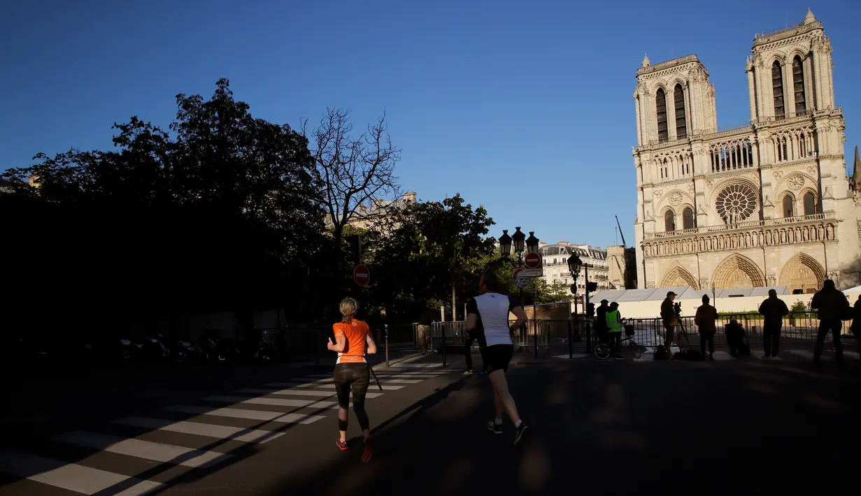 Warga berolahraga di depan Katedral Notre-Dame yang kembali membunyikan lonceng utamanya di Paris, Rabu (15/4/2020). Lonceng utama katedral kembali dibunyikan setelah satu tahun mengalami kebakaran yang sampai mengejutkan seluruh warga dunia. (AP/Christophe Ena)