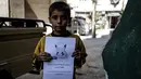 Seorang bocah memegang kertas bergambarkan karakter Pokemon dengan tulisan "Aku di Ghouta Timur di Suriah, datang dan selamatkan Aku", Suriah (22/7). (REUTERS)