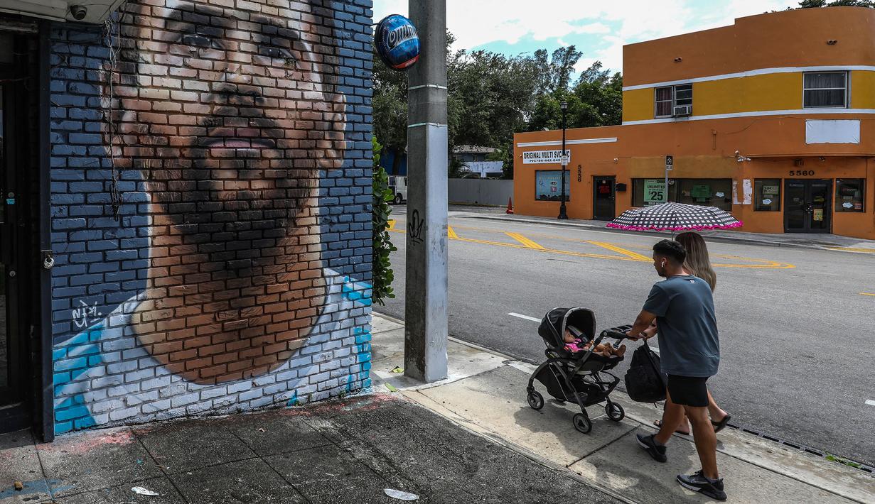 Pejalan kaki melintasi mural wajah Lionel Messi yang berada di salah satu jalan di Miami, Amerika Serikat. Messi memutuskan untuk bergabung dengan klub MLS, Inter Miami, pada Rabu (7/6/2023). (AFP/Giorgio Viera)