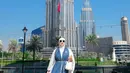 Berpose dengan latar gedung tertinggi di dunia, Burj Khalifa, Tasyi tampil glamor dengan dress putih yang dipadu syal LV warna biru dengan aksen chain belt, dan tas lady Dior warna senada dengan dress-nya. @tasyiiathasyia.