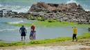 Orang-orang berfoto di antara ganggang hijau yang menyelimuti sebuah teluk di Qingdao, provinsi Shandong, China pada Kamis (11/7/2019). Fenomena alam yang ekstrem ini  memang sudah menjadi agenda tahunan sejak tahun 2008 silam di sepanjang garis pantai Shandong. (AFP Photo)