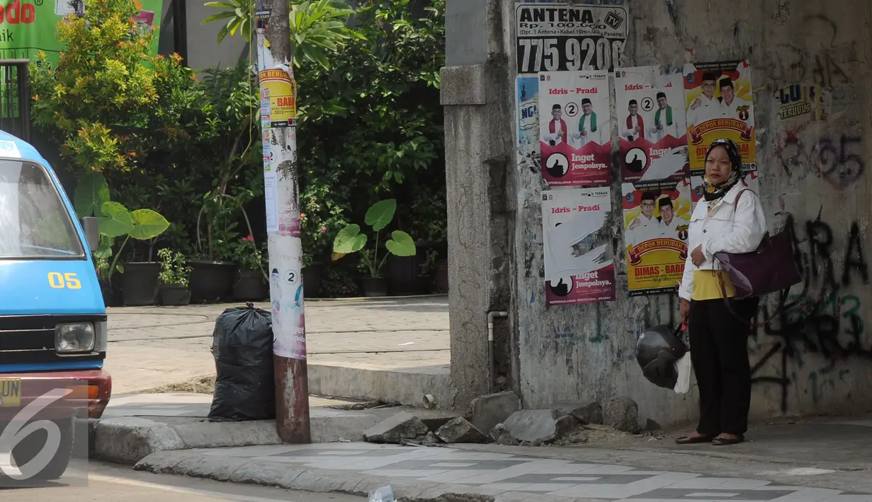 Warga berdiri di depan alat peraga kampanye Pilkada Kota Depok, Jawa Barat, Rabu (2/12). Kota Depok menjadi salah satu daerah yang akan melaksanakan Pilkada serentak pada 9 Desember mendatang. (Liputan6.com/Helmi Fithriansyah)