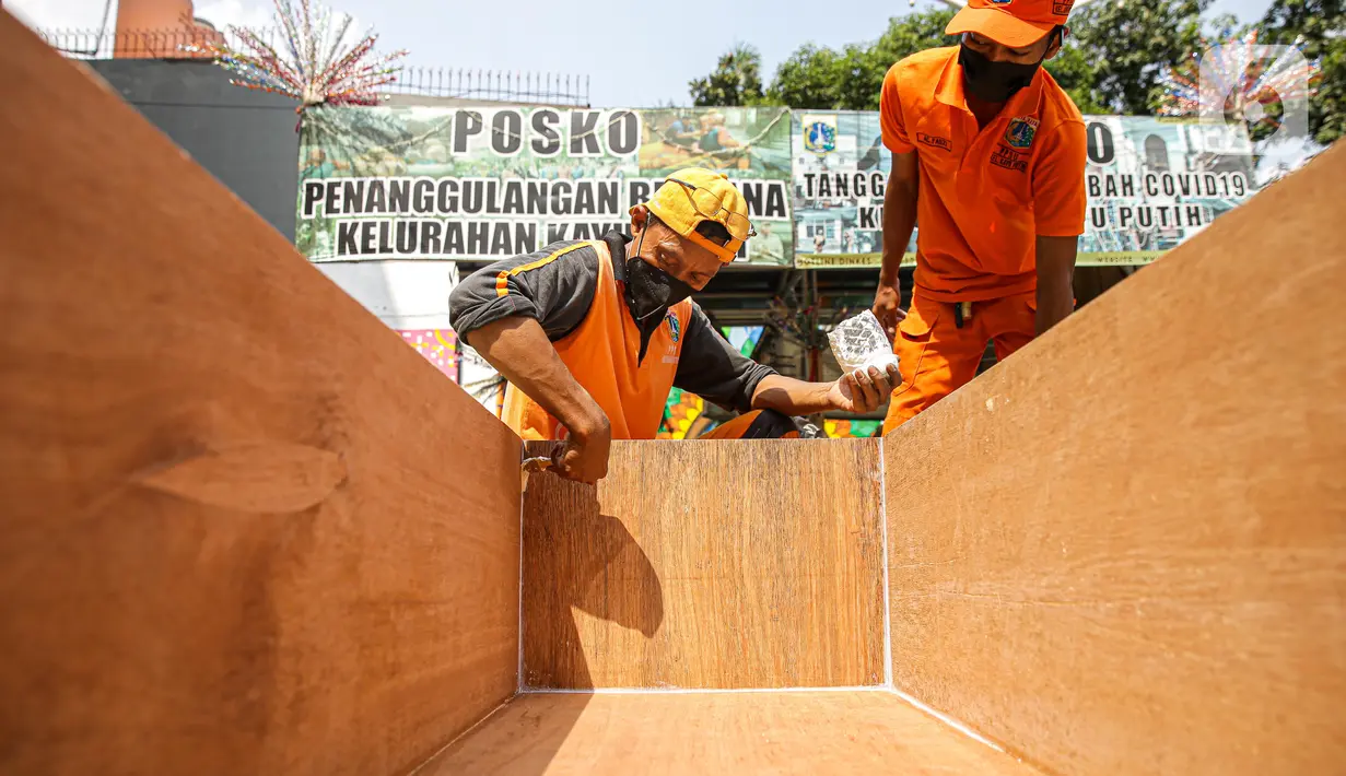 Petugas PPSU mengecat peti jenazah di halaman Kantor Kelurahan Kayu Putih, Jakarta, Selasa, (6/7/2021). Kelurahan Kayu Putih berinisiatif membuat peti jenazah dilatar belakangi warganya yang terkendala ketersediaan peti saat angka kematian COVID-19 meningkat di DKI. (Liputan6.com/Faizal Fanani)