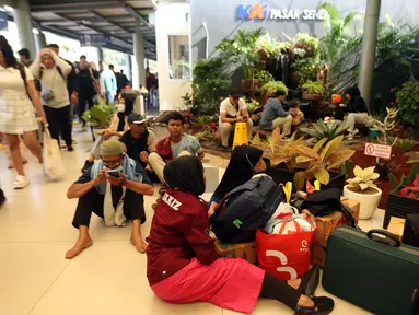 Calon pemudik yang akan menggunakan Kereta Api Jarak Jauh duduk di lantai menanti waktu keberangkatan di Stasiun Pasar Senen, Jakarta, Minggu (7/4/2024). (Liputan6.com/Helmi Fithriansyah)