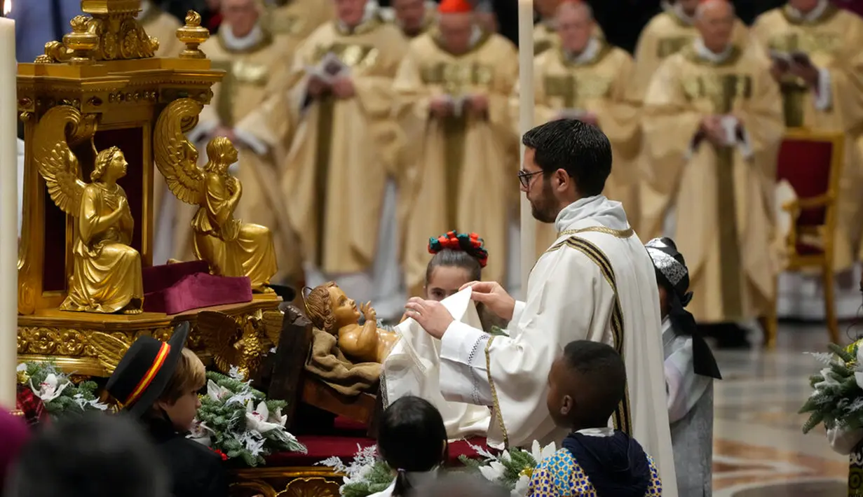 Seorang imam membuka patung Bayi Yesus saat Paus Fransiskus memimpin Misa Malam Natal di Basilika Santo Petrus, Vatikan, 24 Desember 2022. Paus Fransiskus tidak merinci terkait masalah kesehatannya, namun kepala Gereja Katolik mengatakan kepada pers bahwa dia menandatangani surat pengunduran diri jika ada hambatan karena alasan medis dan telah memberikannya kepada menteri luar negeri. (AP Photo/Gregorio Borgia)