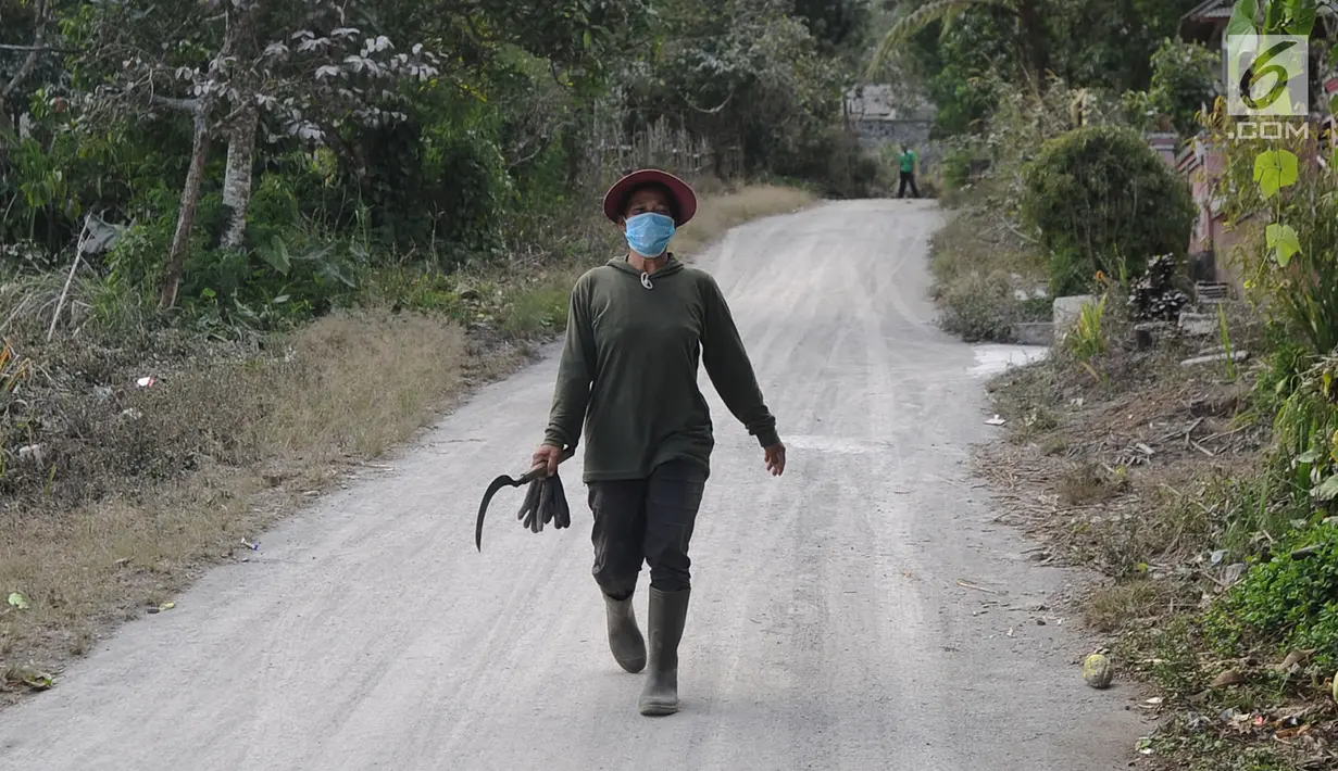 Warga mengenakan masker saat pergi ke ladang di Desa Pempatan, Karangasem, Bali, Sabtu (30/6). Pascaerupsi Gunung Agung, abu vulkanik masih menyelimuti kawasan tersebut. (Merdeka.com/Arie Basuki)
