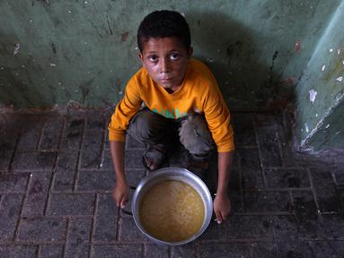 Seorang anak Palestina yang mengungsi duduk di samping sepanci sup miju-miju yang ia terima di sebuah titik distribusi makanan di Kota Gaza di Jalur Gaza utara pada 25 Juli 2025. (Omar AL-QATTAA/AFP)