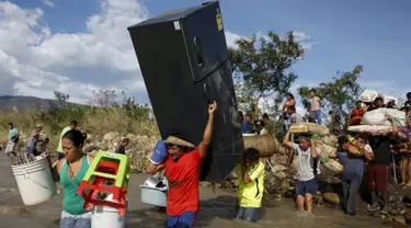 Seorang pria membawa kulkas bersama warga Kolombia lainnya melalui sungai Tachira, Venezuela, (25/8/2015). Pemerintah Venezuela menutup perbatasan dengan Kolombia dan mendeportasi warga Kolombia. (REUTERS/Jose Miguel Gomez)