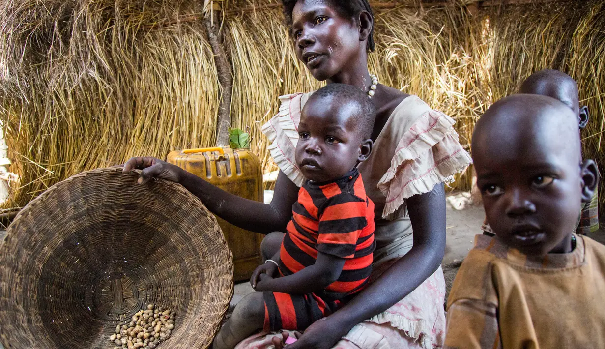 Alissa Lual bersama tiga anaknya menunjukkan persedian makanan di dalam penampungan di Sudan Selatan (22/11). Kini mereka menderita krisis air bersih dan kelaparan karena minimnya persediaan pangan. (AFP Photo/Albert Gonzalez Farran)