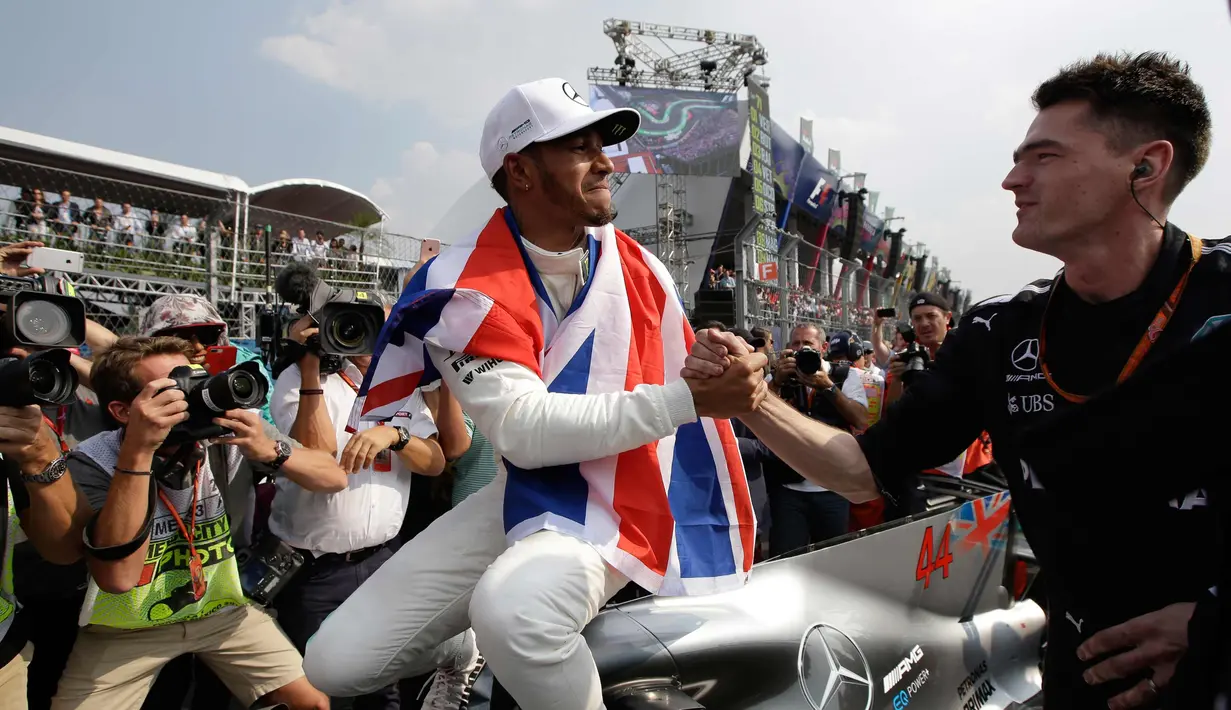 Lewis Hamilton bersalaman dengan salah satu kru timnya saat merayakan kemenangan meraih juara dunia F1 di Autodromo Hermanos Rodrigue, Meksiko (29/10).  Hamilton meraih juara F1 untuk ke empat kalinya. (AP Photo / Moises Castillo)