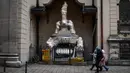 Pejalan kaki berjalan melewati patung-patung yang dibungkus dengan plastik di Katedral Latin di Lviv, 5 Maret 2022. Warga kota Lviv membungkus semua patung untuk melindungi warisan sejarahnya dari kerusakan akibat serangan di tengah konflik Rusia-Ukraina. (Daniel LEAL/AFP)