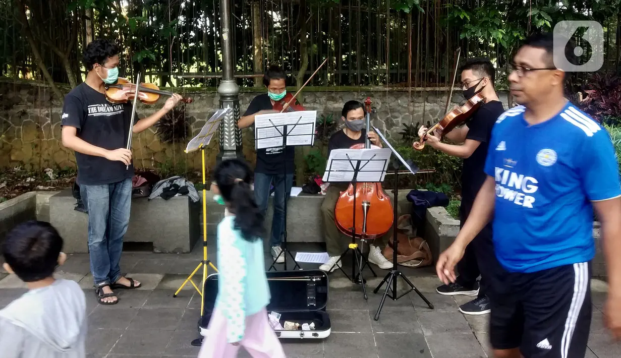 Warga berjalan melewati musisi lokal Bogor yang tengah memainkan musik klasik di pedestrian Kebun Raya, Jalan Pajajaran, Bogor, Jawa Barat, Minggu (14/6/2020). Mereka mengamen untuk memenuhi kebutuhan hidup akibat sepinya job pertunjukan selama pandemi COVID-19. (merdeka.com/Arie Basuki)