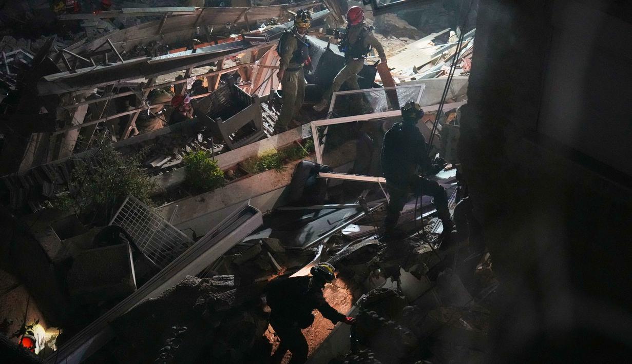 Diduga masih terdapat warga yang terjebak atau hilang di bawah struktur bangunan gedung yang runtuh. Tampak dalam foto, pasukan keamanan Israel dan tim penyelamat melakukan upaya pencarian korban di tengah reruntuhan bangunan tempat tinggal yang dihantam rudal Iran di Haifa, Israel, Minggu, 5 April 2026. (AP Photo/Ariel Schalit)