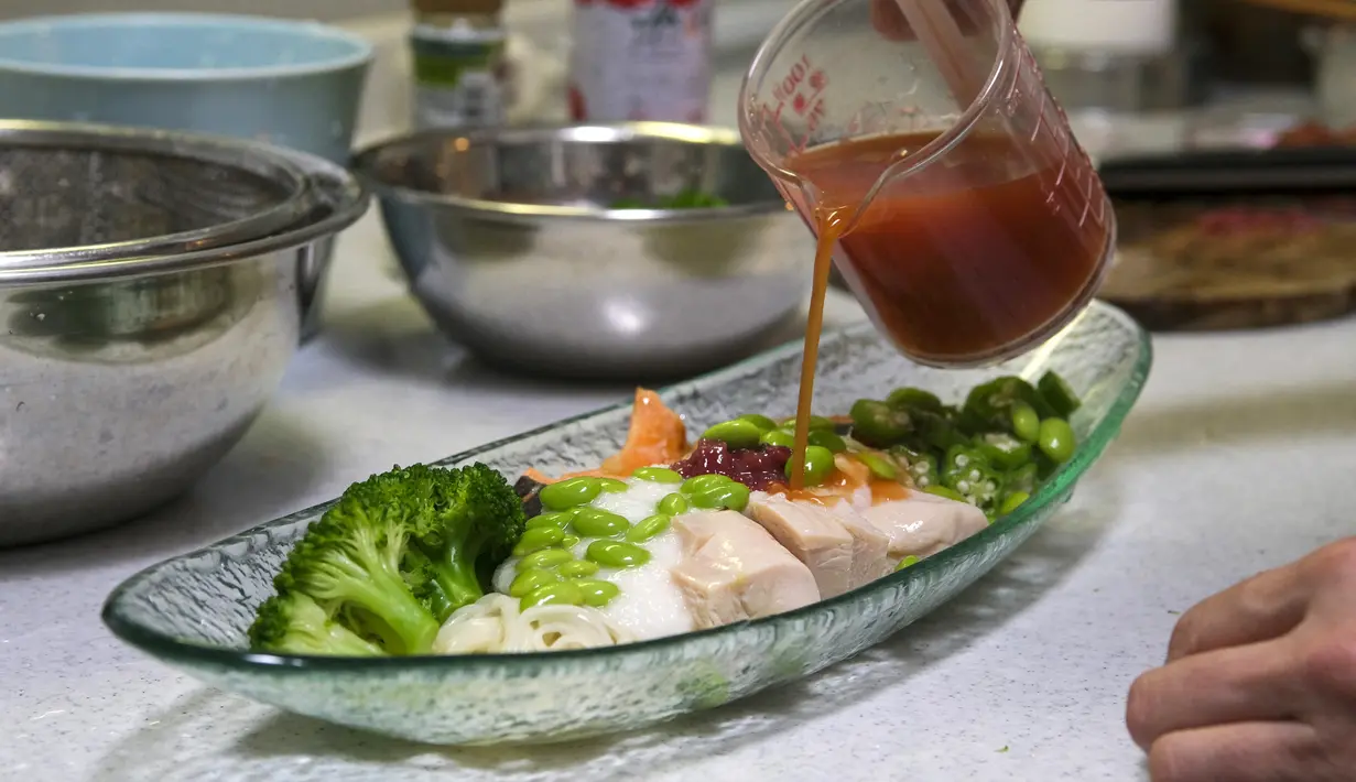 <p>Pemenang kontes resep makanan Desa Olimpiade Tokyo 2020 Yoko Nishimura menuangkan saus ke piring di Tokyo, Jepang, 12 Juli 2021. Desa Olimpiade Tokyo 2020 melarang atlet makan di restoran lokal menyusul aturan ketat terkait virus corona COVID-19. (KAZUHIRO NOGI/AFP)</p>