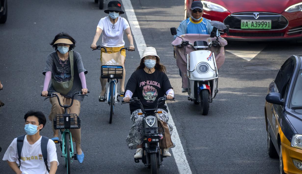 Orang-orang yang memakai masker mengendarai sepeda dan skuter di sepanjang jalan di Beijing, Jumat (8/7/2022). Keputusan mandat vaksin Covid-19 bagi penduduk Beijing menimbulkan pro dan kontra di kalangan penduduk. Banyak dari mereka beranggapan, kebijakan itu akan sangat berdampak pada kehidupan sehari-hari. (AP Photo/Mark Schiefelbein)