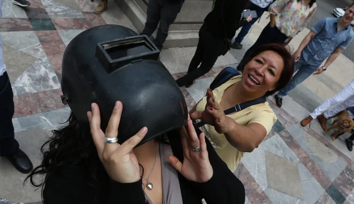 Seorang wanita mengenakan helm las untuk melihat gerhana matahari parsial di Mexico City, Senin (21/8). Gerhana matahari total terjadi di 14 negara bagian AS, sementara lainnya mengalami gerhana matahari parsial. (Gustavo Martinez Contreras/AP)