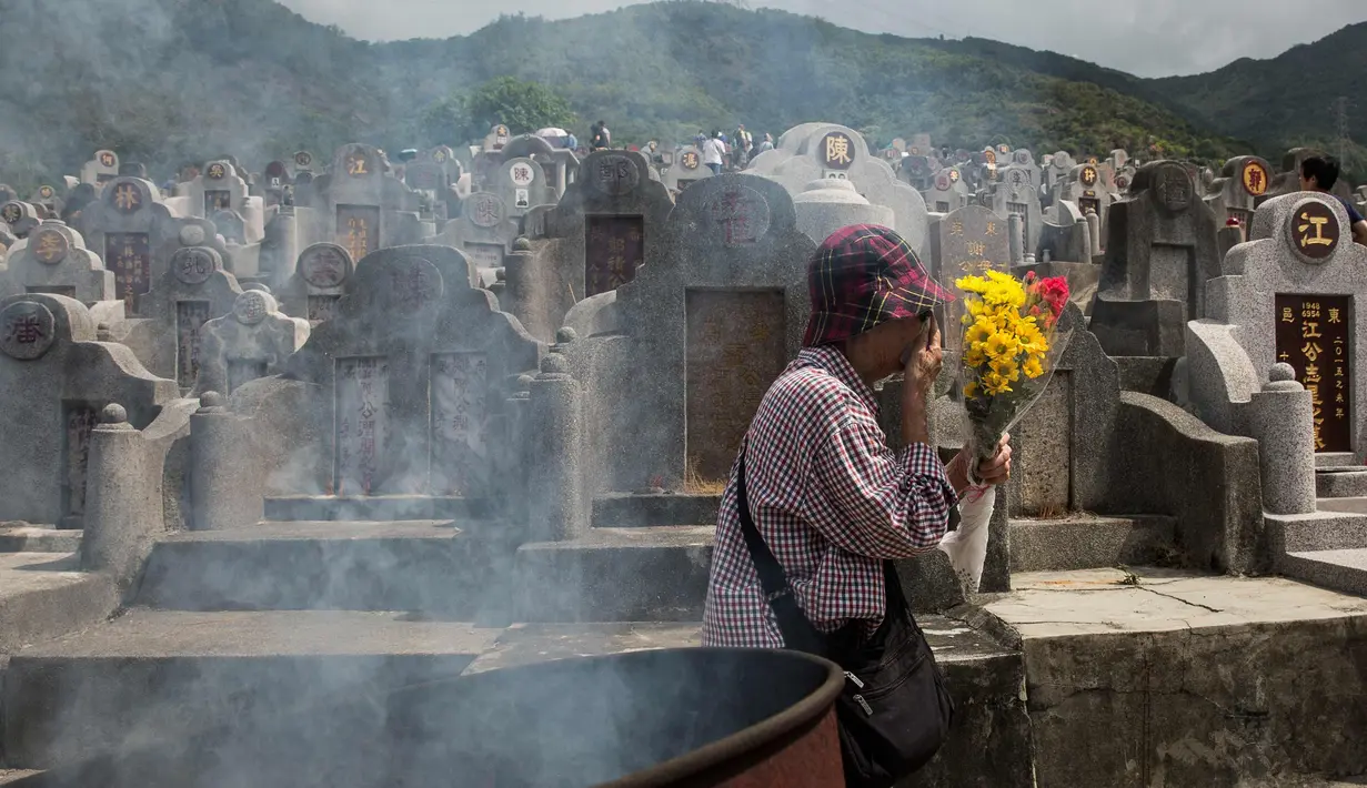 Seorang wanita membawa bunga selama festival Qingming di pemakaman di Hong Kong (5/4). Festival Qingming atau dikenal sebagai Hari Pembersihan Makam untuk menghormati orang yang dicintainya yang telah tiada. (AFP Photo/Isaac Lawrence)