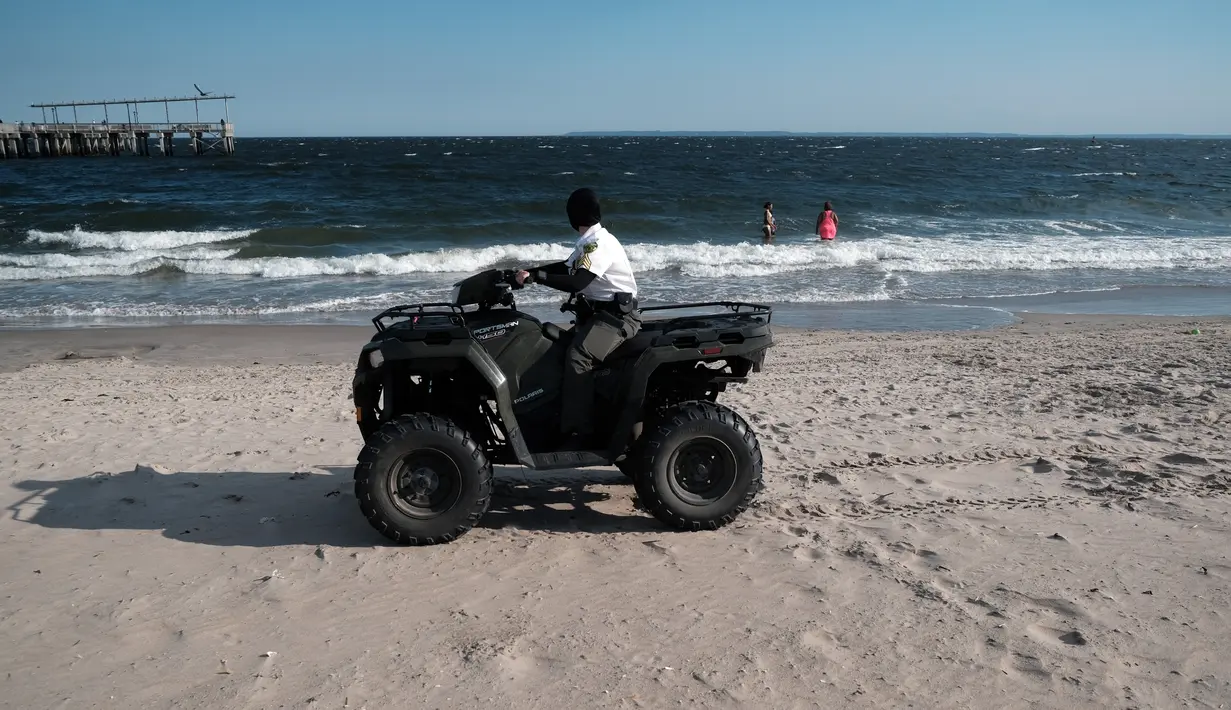 Seorang pegawai taman kota melihat para perenang di Coney Island, salah satu tujuan pantai paling populer di wilayah Brooklyn di New York City (29/6/2022). Kota New York menghadapi kekurangan penjaga pantai di kolam renang kota dan pantai tahun ini, memaksa beberapa daerah untuk membatasi waktu berenang. (Spencer Platt/Getty Images/AFP)