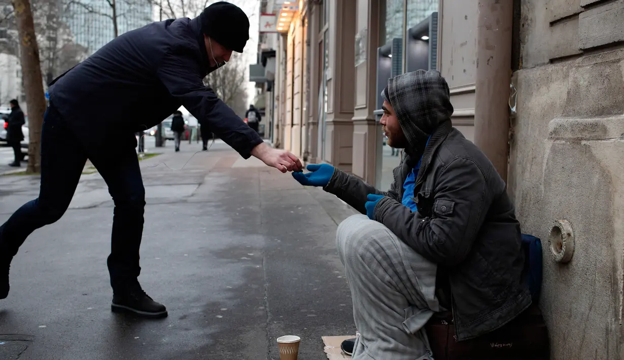 Seorang tunawisma menerima sejumlah uang saat dia duduk di jalanan di Paris, Senin (5/2). (AP Photo / Francois Mori)