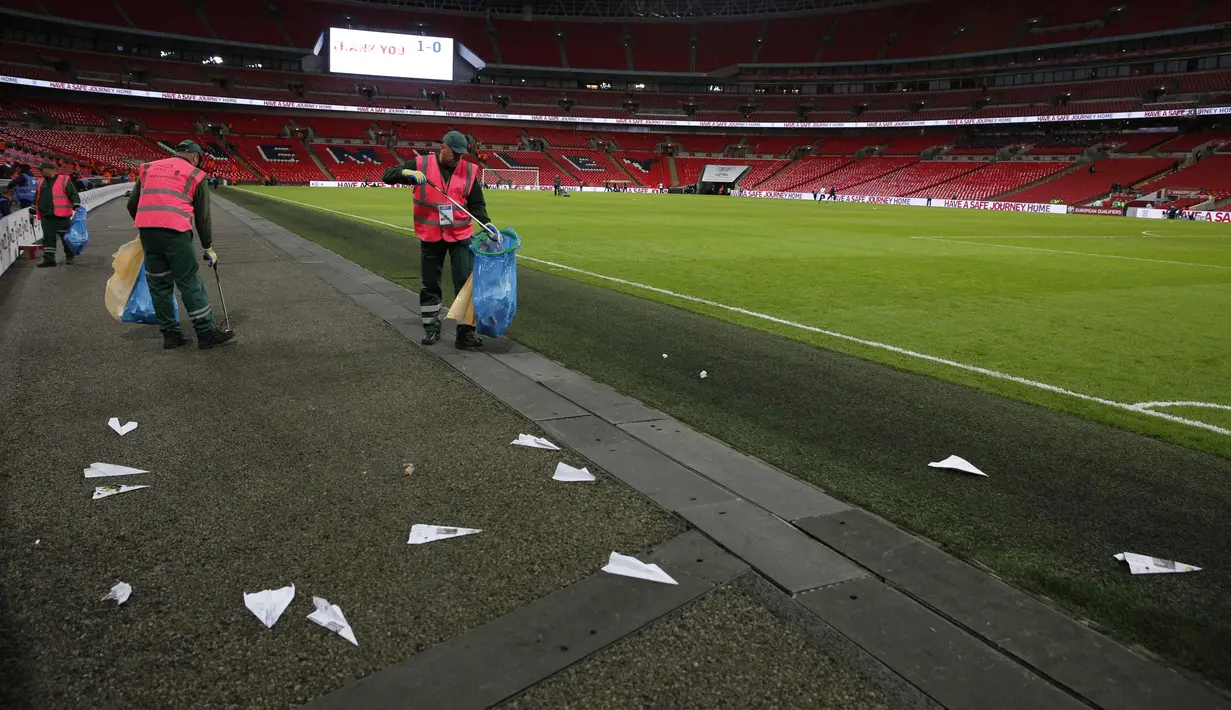 Petugas mengumpulkan pesawat kertas selama pertandingan Inggris melawan Slovenia di stadion Wembley, London, (5/10). Suporter melemparkan pesawat kertas sebagai solusi mengatasi kebosanan pertandingan. (AFP Photo/Adrian Dennis)