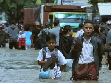 Pelajar berusaha melintasi genangan air ketika banjir merendam Jalan KH Hasyim Ashari, Ciledug, Kota Tangerang, Selasa (10/2/2015). (Liputan6.com/Andrian M Tunay)