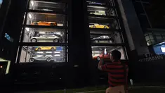 Seorang pria mengambil gambar vending machine atau mesin penjual otomatis berisi mobil-mobil mewah di gedung Autobahn Motors, Singapura, Kamis (18/5). Vending machine berbentuk bangunan bertingkat itu dapat menampung hingga 60 mobil. (ROSLAN RAHMAN/AFP)