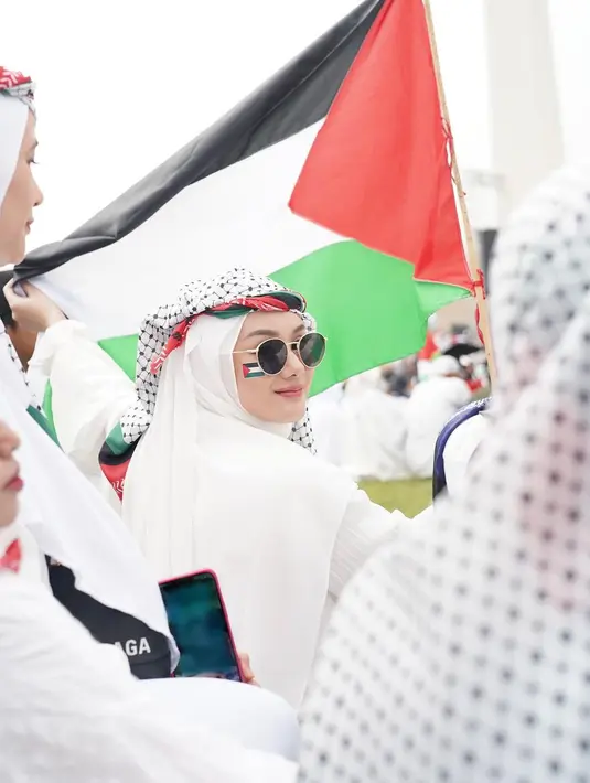 Dinda Hauw juga turut turun ke jalan di Monas untuk aksi damai bela Palestina bersama sang suami Rey Mbayang. Di akun Instagramnya, Dinda Hauw memperlihatkan dirinya yang mengenakan outfit serba putih, melilitkan sorban dan syal berwarna bendera Palestina di kepalanya, stiker bendera Palestina di pipinya, dan sunglasses. [Foto: Instagram/dindahw]