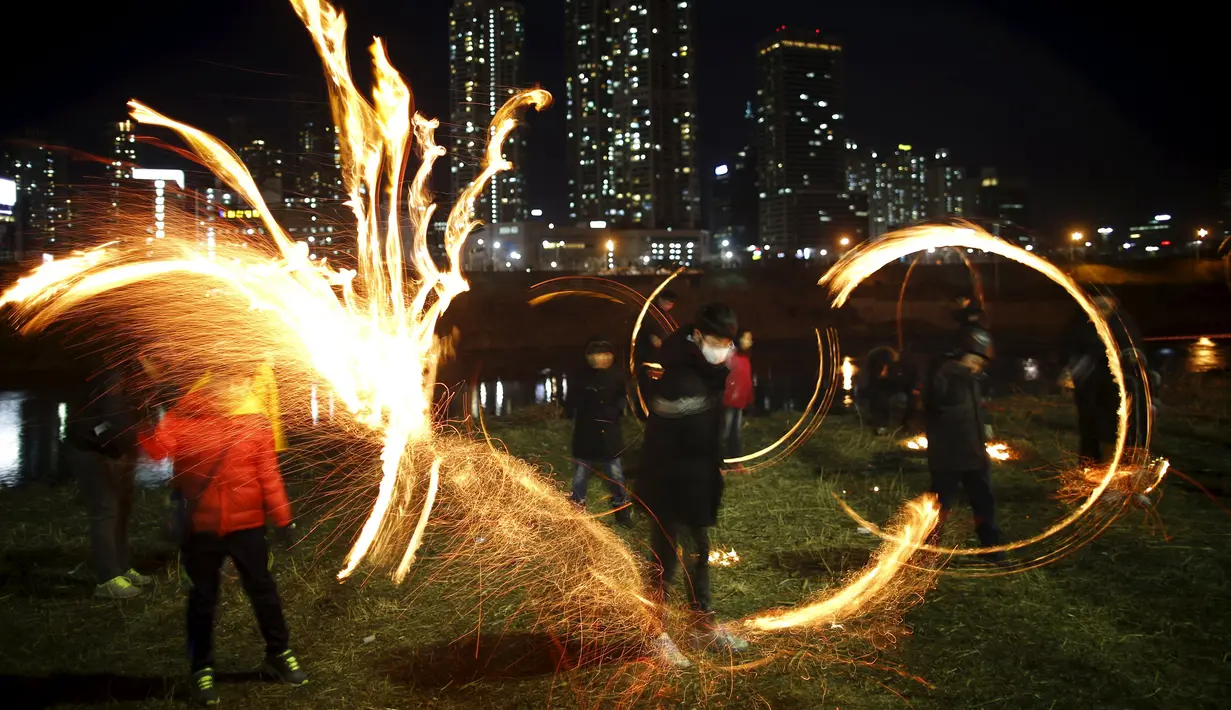 Sejumlah anak memutarkan kaleng berisi kayu yang dibakar jelang perayaan "Jeongwol Daeboreum"di sebuah taman di Seoul, Korea Selatan, Minggu (21/2). Tarian api ini merupakan bagian dari perayaan Imlek ala Korea. (REUTERS/Kim Hong-Ji)