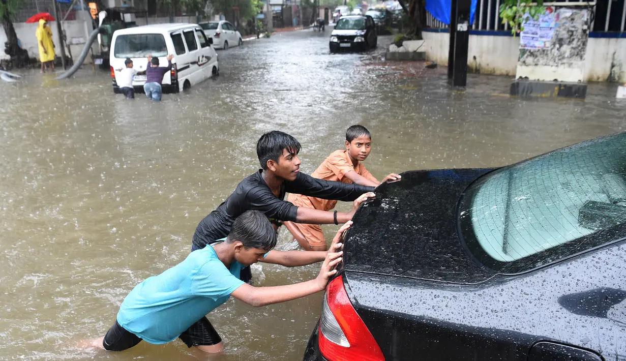 Sejumlah anak mendorong sebuah mobil yang mogok akibat melintasi banjir saat hujan deras di Mumbai, India (9/7). Mumbai dan daerah pinggiran lainnya telah mengalami hujan lebat semalaman yang mengakibatkan banjir. (AFP Photo/Indranil Mukherjee)