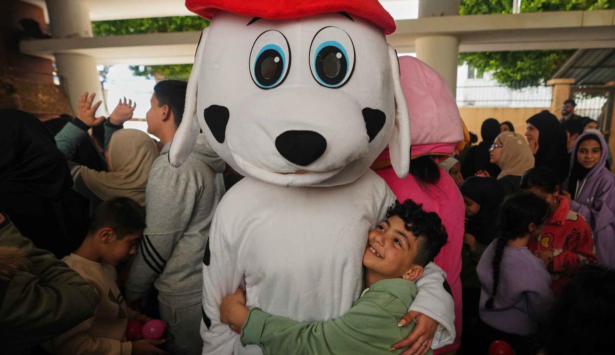 Meski dalam kondisi perang, beberapa pengungsi tetap berupaya menghadirkan kegembiraan, terutama untuk anak-anak, dalam menyambut hadirnya Hari Raya Idulfitri. Tampak dalam foto, seorang anak memeluk seseorang yang mengenakan kostum saat para sukarelawan menyiapkan bingkisan makanan dan manisan Idulfitri untuk keluarga pengungsi yang merayakan hari raya jauh dari rumah mereka, di sebuah universitas negeri yang diubah menjadi tempat penampungan setelah serangan udara Israel di Beirut, Lebanon, Jumat 20 Maret 2026. (AP Photo/Hassan Ammar)