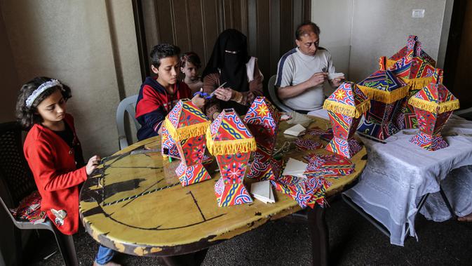 Anggota keluarga Palestina al-Yaqoubi berkumpul di sekitar meja membuat lentera bulan suci Ramadan untuk dijual selama penerapan lockdown di Khan Yunis, di Jalur Gaza selatan pada 15 April 2020. Karena pandemi Covid-19, keadaan berubah dan tradisi Ramadan pun tidak akan ada. (SAID KHATIB / AFP)