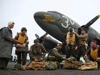 Para peraga Perang Dunia Kedua berpose di samping C-47, sebuah pesawat yang mengangkut pasukan penerjun payung di atas zona penerjunan di Normandia, Prancis, di North Weald Airfield di Epping, sebelah timur London, pada 31 Mei 2024. (HENRY NICHOLLS/AFP)