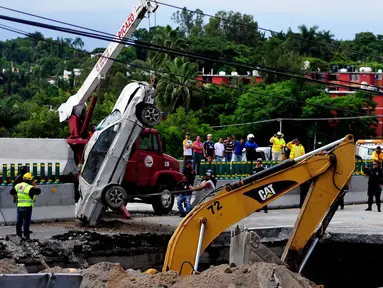 Tim penyelamat menggunakan derek untuk mengangkat sebuah mobil yang tertelan ke dasar lubang di jalan raya Meksiko-Cuenava, Meksiko, Rabu (12/7). Lubang yang tiba-tiba muncul itu membunuh seorang ayah dan putranya yang tengah berkendara. (AP/Tony Rivera)