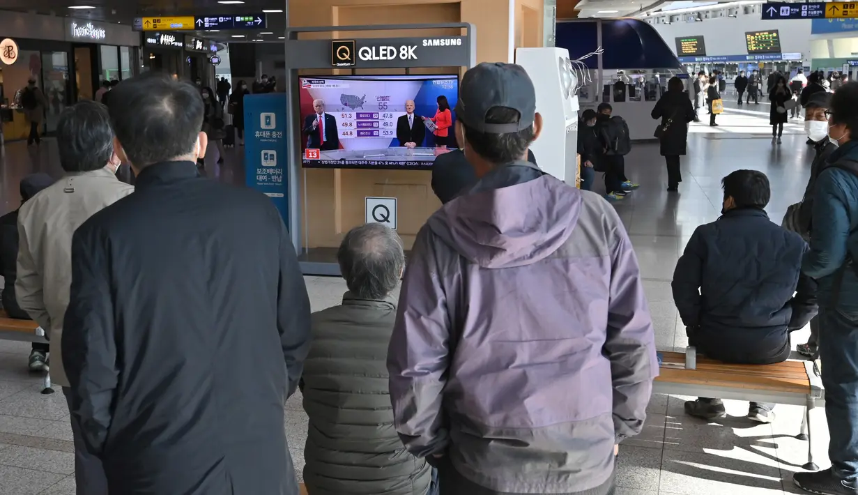 Orang-orang menonton program berita televisi tentang pemilihan presiden (pilpres) AS yang menampilkan gambar Presiden Donald Trump (kiri) dan calon presiden dari Partai Demokrat Joe Biden (kanan), di sebuah stasiun kereta api di Seoul, Korea Selatan pada Rabu (4/11/2020). (Photo by Jung Yeon-je/AFP)