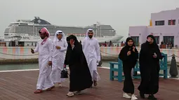 Pria dan wanita berjalan selama ajang Piala Dunia 2022 Qatar di Distrik Mina Doha pada 10 Desember 2022. Letaknya yang sempurna di dekat perairan Doha di mana Anda dapat melihat pemandangan yang ditempatkan kapal pesiar seperti MSC World Europa, berfungsi sebagai pilihan akomodasi bagi penggemar sepak bola. (AFP/Christina Assi)