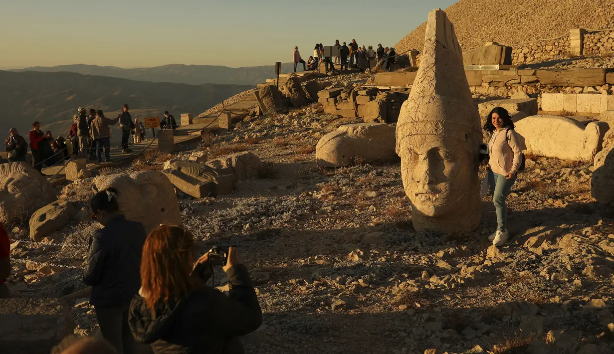 Gambar pada 23 September 2019 memperlihatkan wisatawan berfoto di Gunung Nemrut, Provinsi Adiyaman di Turki bagian tenggara. Pengunjung juga bisa mengagumi patung kepala Dewa yang bervariasi dari wajah manusia hingga pahatan singa yang berfungsi sebagai penjaga makam. (AP/Emrah Gurel)