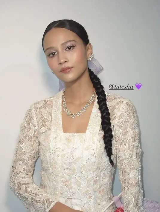 Lutesha tampil dengan kebaya putih brokat dipadukan kalung silver. Dengan gaya rambut kembang belakang, serta riasan wajah fresh dengan eyeshadow ungu. [@vagueskin]