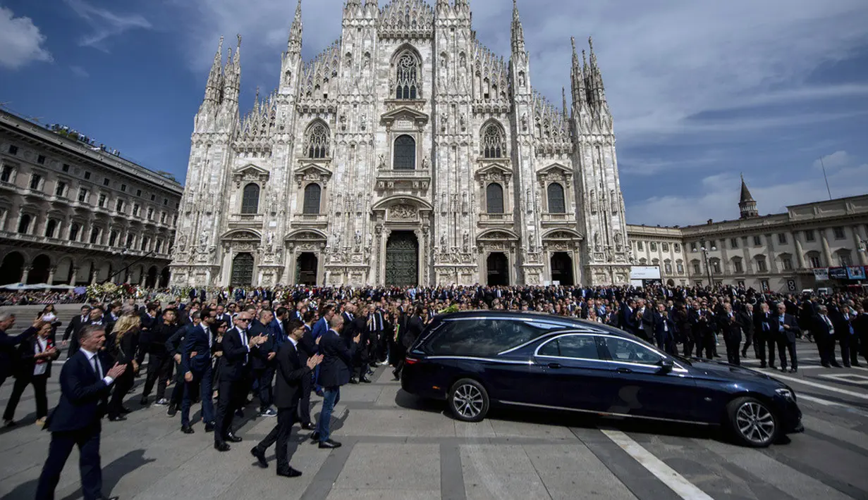 <p>Kerumunan massa mengibarkan bendera klub sepak bola AC Milan sambil meneriakkan "Silvio, Silvio" saat peti matinya dibawa ke dalam Katedral Gotik Milan. Peti mati Berlusconi dikawal oleh polisi Carabinieri. (Claudio Furlan/LaPresse via AP)</p>