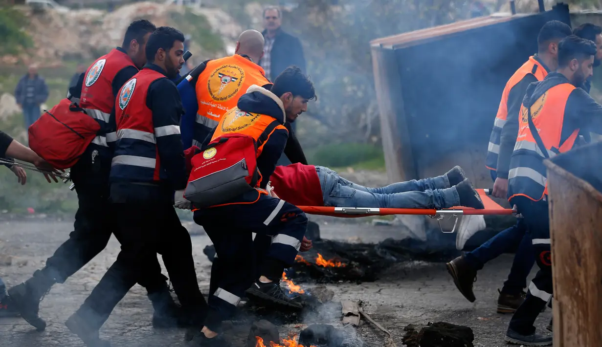 Petugas medis Palestina mengevakuasi seorang demonstran yang terluka dalam bentrokan saat melakukan demonstrasi menolak pengakuan Yerusalem sebagai ibu kota Israel di kota Ramallah, Palestina (16/3). (AFP Photo/Abbas Momani)