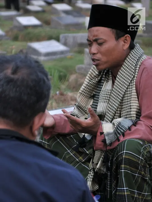 Seorang pria bernama Ma'ruf memimpin doa 'Talkin' untuk peziarah di TPU Kemiri, Rawamangun, Jakarta, Selasa (15/5). Pria yang bekerja sebagai guru ngaji ini bisa mendapatkan ratusan ribu rupiah dari hasil pembaca doa musiman. (Merdeka.com/Iqbal S Nugroho)