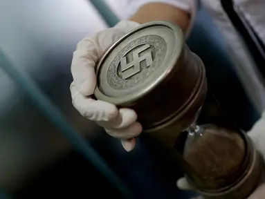 Anggota polisi federal memegang jam pasir dengan tanda Nazi di markas Interpol di Buenos Aires, Argentina, (16/6).  Polisi menemukan 75 koleksi artefak Nazi di ruangan tersembunyi di sebuah rumah kawasan Buenos Aries. (AP Photo/Natacha Pisarenko)